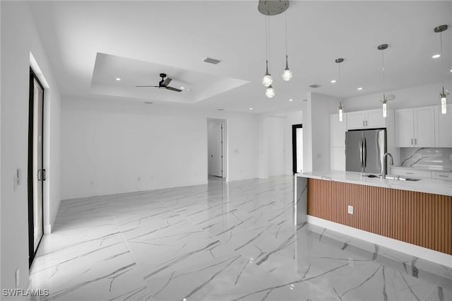 kitchen with white cabinets, sink, a tray ceiling, decorative light fixtures, and stainless steel refrigerator