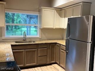 kitchen featuring sink, white cabinetry, light stone counters, black fridge, and light wood-type flooring