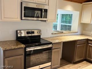 kitchen featuring light stone counters, white cabinetry, stainless steel appliances, and light hardwood / wood-style floors