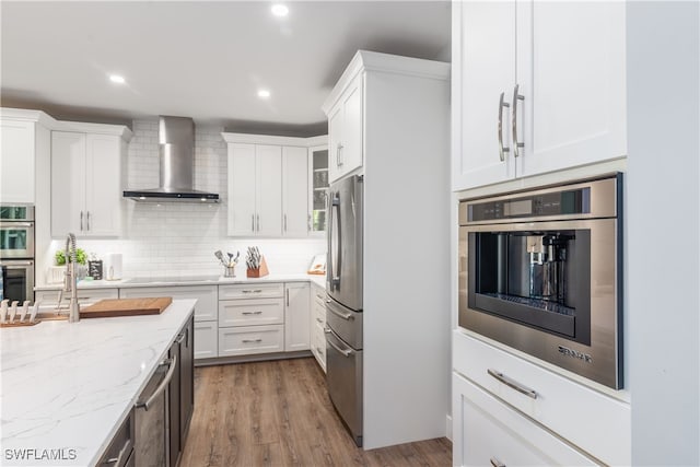 kitchen featuring tasteful backsplash, light stone countertops, stainless steel appliances, wall chimney range hood, and white cabinetry