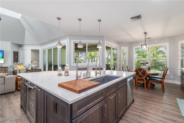 kitchen with dark brown cabinetry, visible vents, open floor plan, light wood-style floors, and a sink