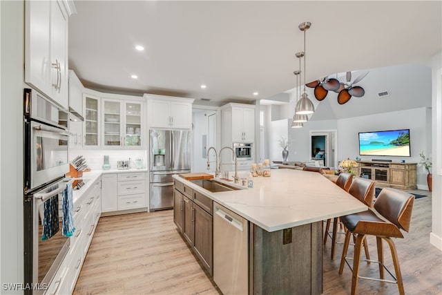 kitchen with a breakfast bar area, a kitchen island with sink, a sink, white cabinets, and appliances with stainless steel finishes