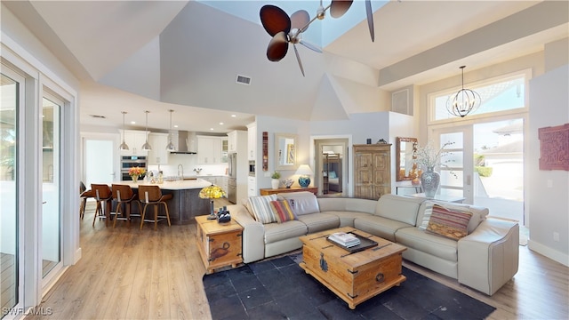 living room featuring visible vents, wood finished floors, high vaulted ceiling, baseboards, and ceiling fan with notable chandelier