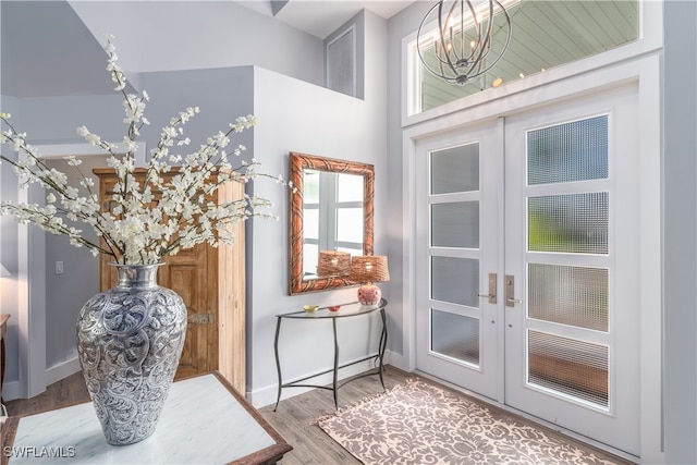 doorway with hardwood / wood-style floors, a chandelier, a towering ceiling, and french doors