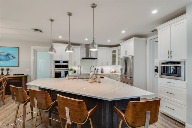 kitchen featuring stainless steel appliances, white cabinetry, wall chimney range hood, and decorative backsplash