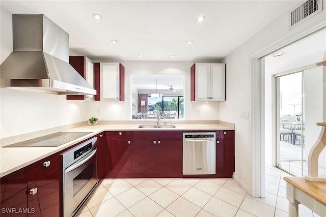 kitchen featuring ceiling fan, sink, wall chimney exhaust hood, light tile patterned floors, and appliances with stainless steel finishes