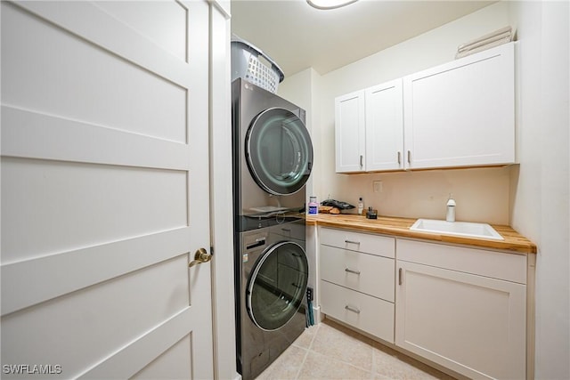 clothes washing area featuring stacked washer / drying machine, cabinets, light tile patterned floors, and sink