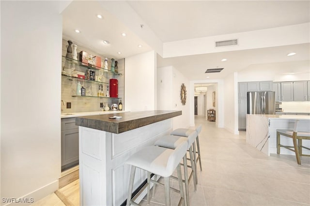 bar with wooden counters, sink, decorative backsplash, stainless steel fridge, and gray cabinets