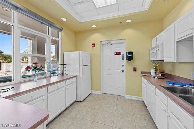 kitchen with sink, white cabinets, white appliances, a tray ceiling, and light tile patterned floors