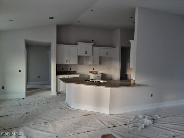 kitchen with kitchen peninsula, high vaulted ceiling, white cabinetry, and dark stone countertops