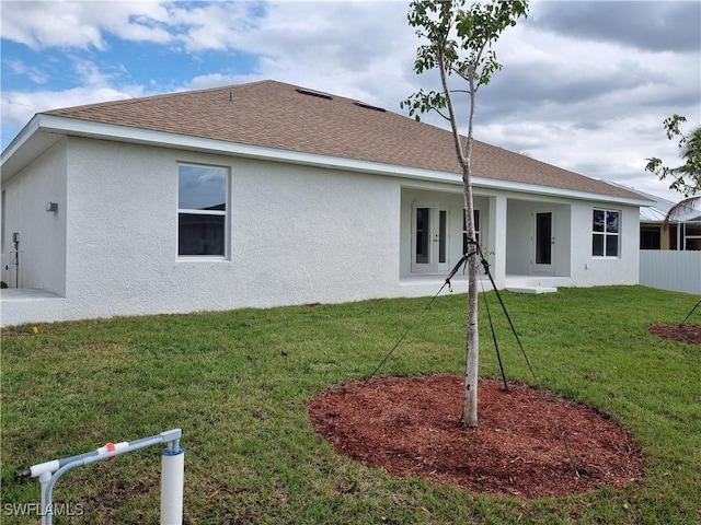 back of house with a yard, roof with shingles, fence, and stucco siding