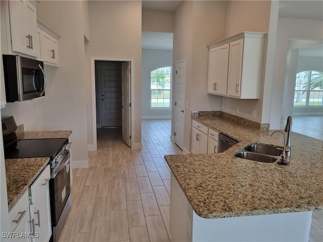 kitchen with baseboards, a peninsula, stainless steel appliances, white cabinetry, and a sink