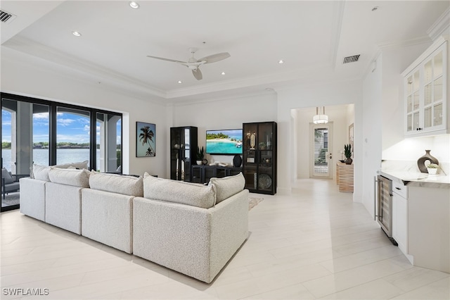 living room featuring ceiling fan, a water view, wine cooler, and a tray ceiling