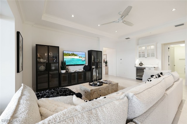 living room with ceiling fan, a raised ceiling, ornamental molding, and beverage cooler