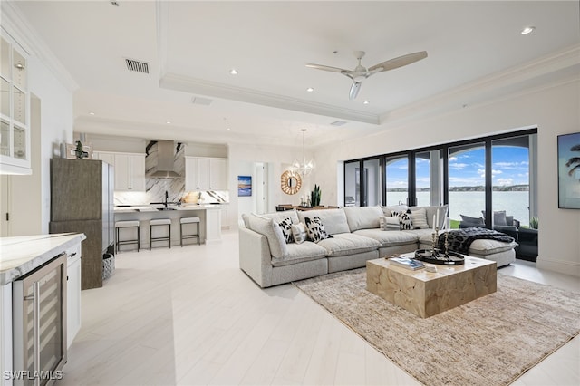 living room featuring ceiling fan with notable chandelier, crown molding, sink, a water view, and wine cooler