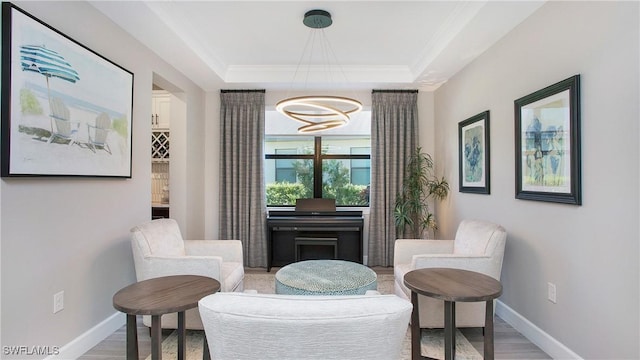 sitting room with a raised ceiling, wood-type flooring, and a chandelier