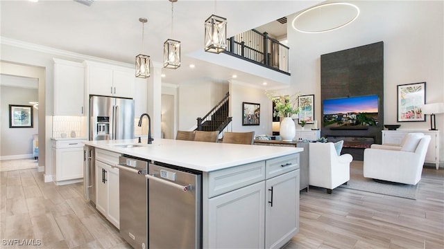 kitchen with white cabinets, stainless steel fridge, pendant lighting, and an island with sink