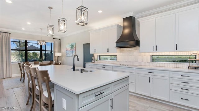 kitchen featuring a center island with sink, white cabinets, decorative light fixtures, and custom exhaust hood