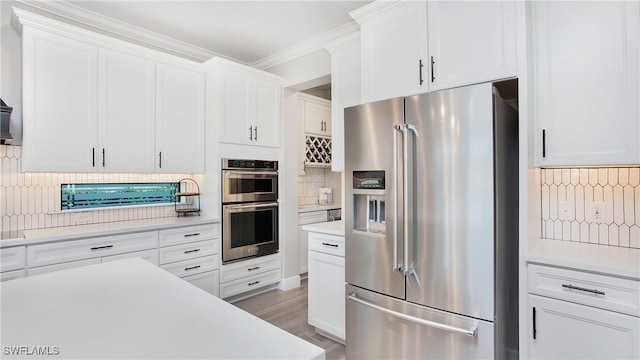 kitchen featuring backsplash, crown molding, wood-type flooring, white cabinets, and appliances with stainless steel finishes