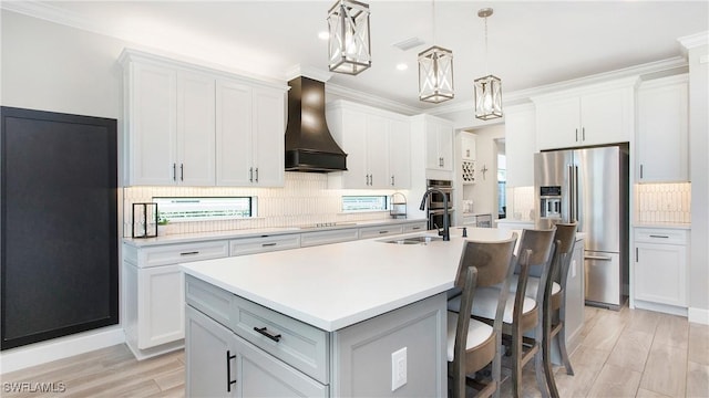 kitchen featuring pendant lighting, a center island with sink, white cabinets, custom exhaust hood, and appliances with stainless steel finishes