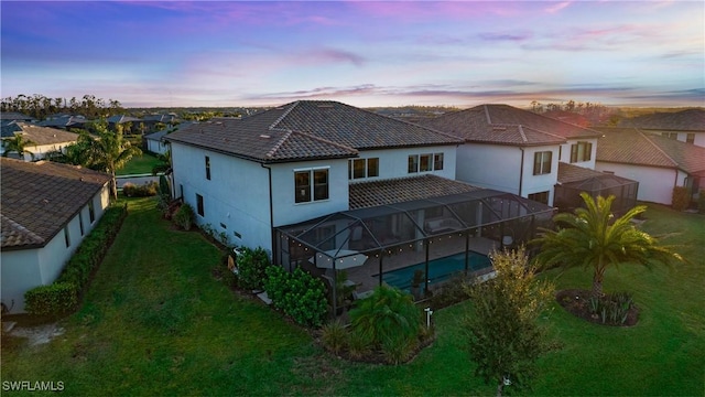 back house at dusk featuring a lawn and glass enclosure