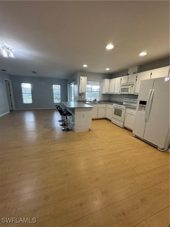 kitchen featuring a breakfast bar area, white cabinetry, white appliances, a healthy amount of sunlight, and light hardwood / wood-style floors