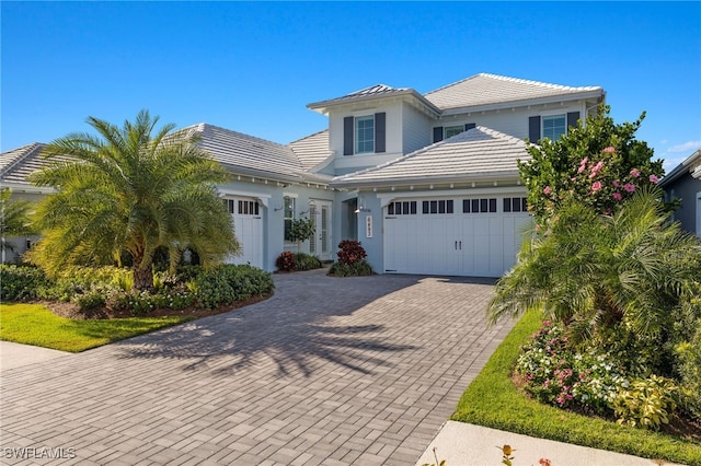 view of front facade with a tiled roof, decorative driveway, a garage, and stucco siding