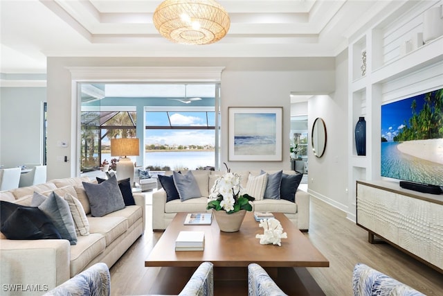 living room featuring built in features, wood finished floors, baseboards, ornamental molding, and a raised ceiling