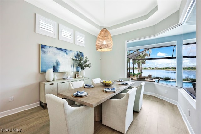 dining space with a tray ceiling, baseboards, light wood-style floors, and a water view