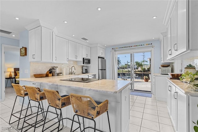 kitchen with white cabinets, a breakfast bar, backsplash, and appliances with stainless steel finishes