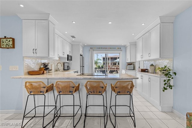 kitchen with white cabinets, a kitchen bar, kitchen peninsula, and stainless steel appliances