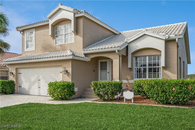 mediterranean / spanish house featuring an attached garage, a front yard, a tile roof, and stucco siding