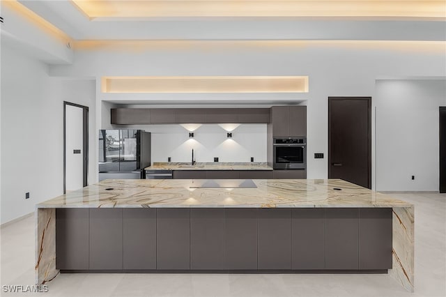 kitchen with sink, light stone counters, a spacious island, and black appliances