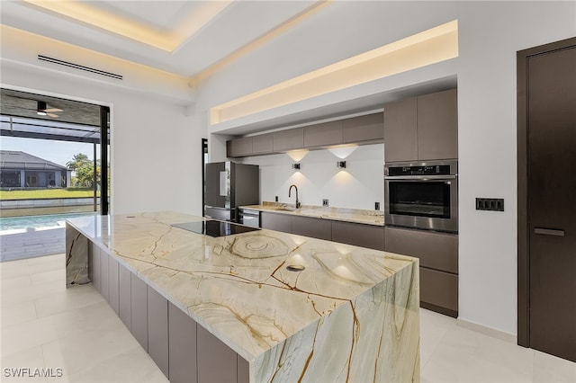 kitchen featuring gray cabinetry, sink, stainless steel appliances, light stone counters, and a spacious island