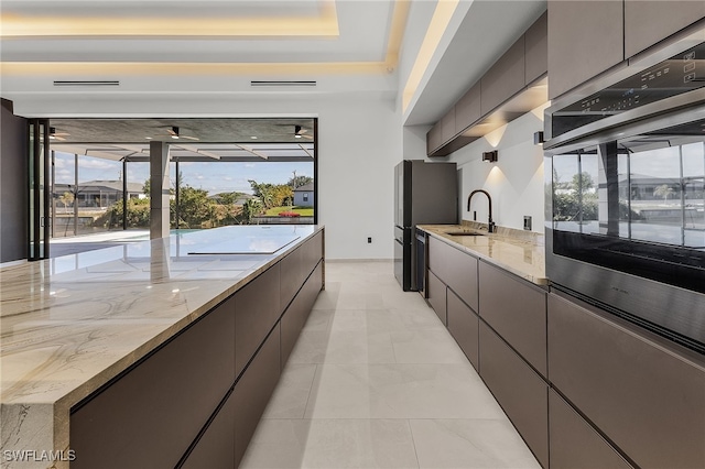 kitchen with light stone countertops, light tile patterned floors, a raised ceiling, and sink