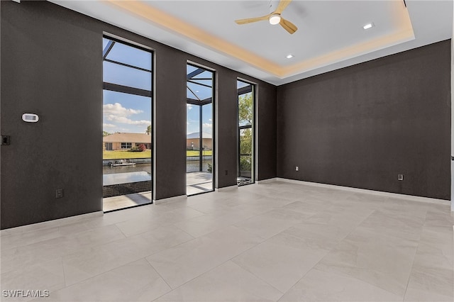 spare room featuring a tray ceiling, ceiling fan, and a water view