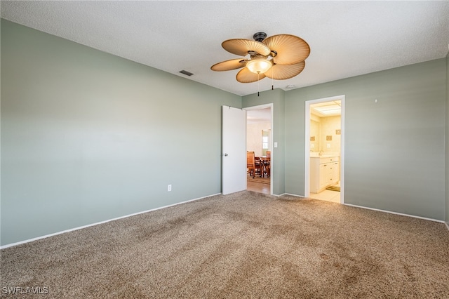 unfurnished bedroom with light carpet, a textured ceiling, connected bathroom, and ceiling fan