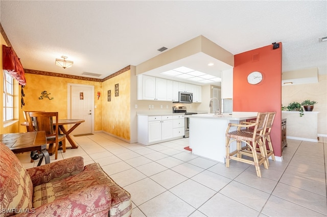 kitchen with kitchen peninsula, appliances with stainless steel finishes, a breakfast bar, white cabinets, and light tile patterned flooring