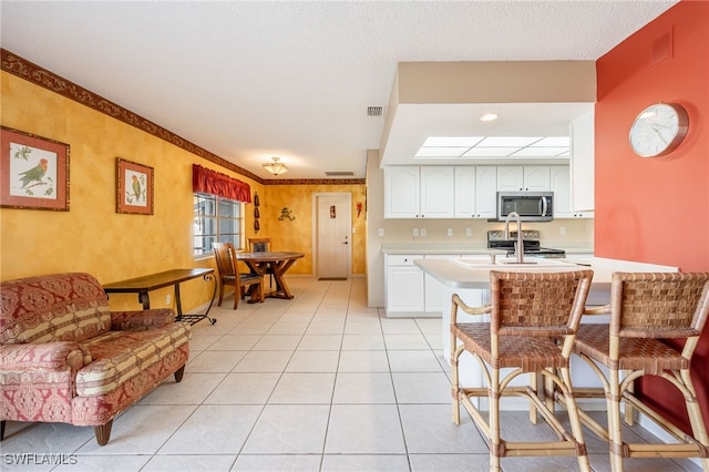 kitchen featuring light tile patterned floors, kitchen peninsula, a breakfast bar, white cabinets, and appliances with stainless steel finishes