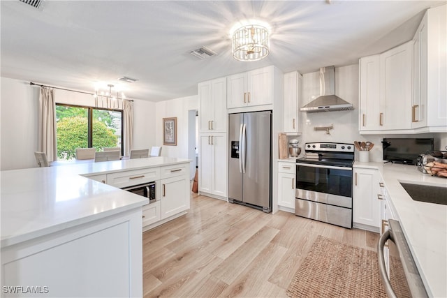 kitchen featuring an inviting chandelier, stainless steel appliances, white cabinetry, and wall chimney exhaust hood