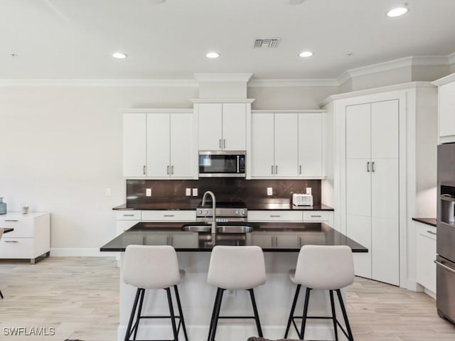 kitchen with a kitchen island with sink, a breakfast bar, white cabinets, and appliances with stainless steel finishes