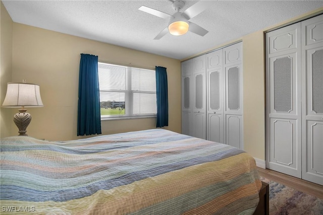 bedroom featuring wood-type flooring, a textured ceiling, two closets, and ceiling fan