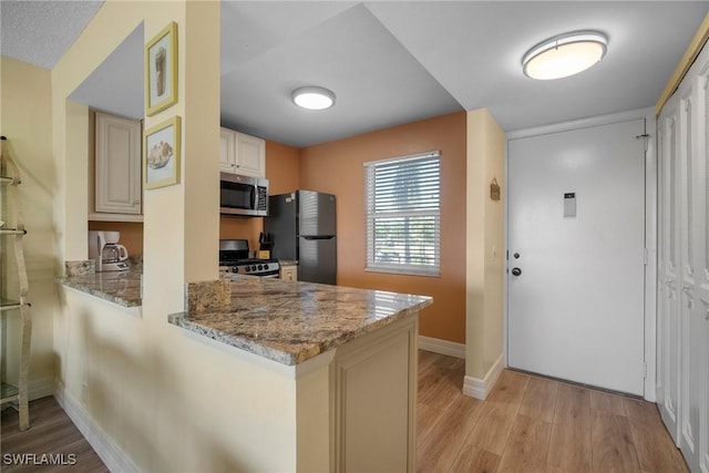 kitchen with light stone countertops, kitchen peninsula, light hardwood / wood-style flooring, and black appliances