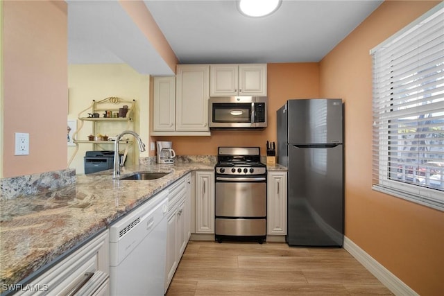 kitchen with sink, light wood-type flooring, light stone countertops, and stainless steel appliances