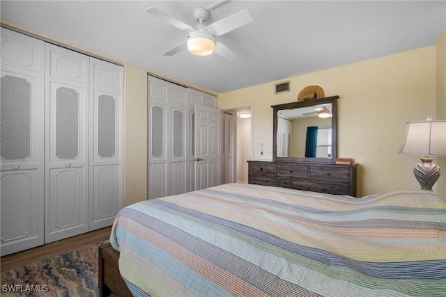 bedroom with ceiling fan, dark wood-type flooring, and two closets