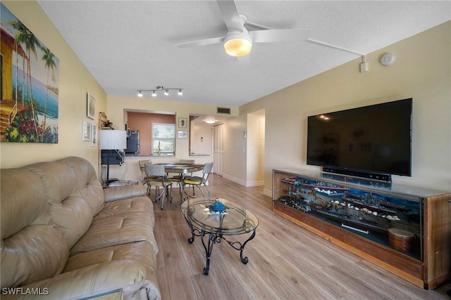 living room featuring ceiling fan, a textured ceiling, and light hardwood / wood-style flooring