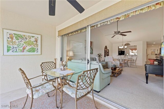 carpeted dining space with a textured wall, vaulted ceiling, and ceiling fan with notable chandelier