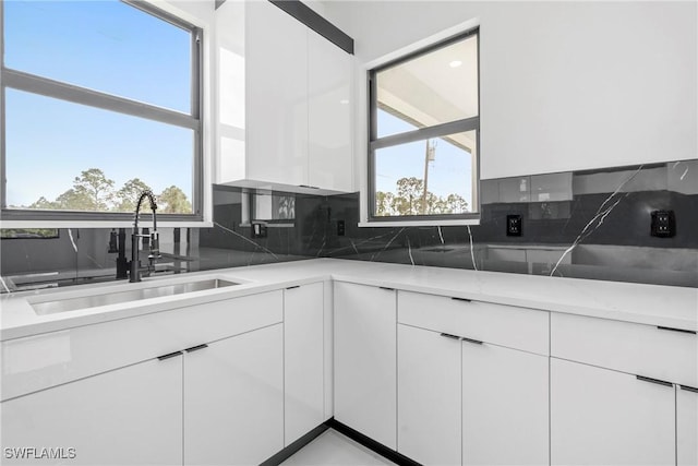 kitchen featuring white cabinets, tasteful backsplash, light stone countertops, and sink