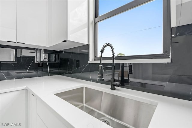 kitchen featuring white cabinets, backsplash, light stone counters, and sink