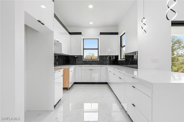 kitchen with tasteful backsplash, kitchen peninsula, white cabinetry, and plenty of natural light